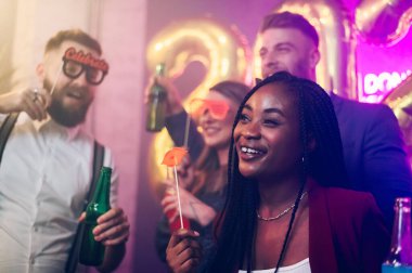 Klüpte çılgın bir gece geçirirken şık ve çekici çok ırklı arkadaşlar yılbaşı partisini kutluyorlar. Saçları komik fotoğraflarla örülü Afrikalı Amerikalı bir kadına odaklan..