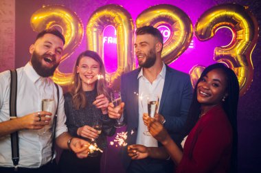 Güzel farklı arkadaşlar kulüpteki yeni yıl partisinde eğleniyorlar. Maytap ve şampanyayla kutlama yaparken eğlenen gençlerin portresi. Gözlüklü çok ırklı arkadaşlar.