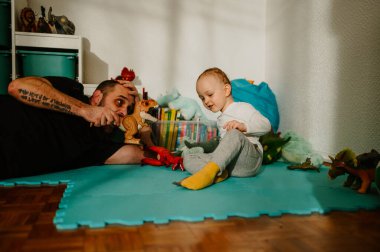Neşeli küçük bir çocuk evde babasıyla dinozor oyuncaklarıyla eğlenceli bir oyun oynuyor. Aile oyun zamanı. Sağlıklı yetiştirme ve geliştirme konsepti. Eğlenceli bir baba oğluyla oyun oynuyor..