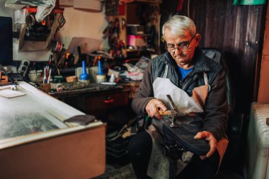 Kıdemli bir zanaatkârın portresi. Ayakkabıcı atölyesinde oturuyor ve eski bir bot tamiri için çekiç kullanıyor. Eski bir kunduracı atölyesinde oturuyor, çekiçle tabana vuruyor ve tamir ediyor..