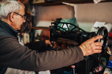 Ayakkabıcı, ayakkabıcısının atölyesinde dikiş makinesi dikiyor. Kıdemli bir ayakkabıcının, ayakkabı ve ayakkabı tamir atölyesinde dikiş makinesi kullanmasının profili. Zanaatkar.