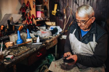 Yaşlı bir zanaatkar ayakkabı tamirhanesinde oturuyor ve makasıyla deri parçaları kesiyor. Ayakkabıcı atölyesinde otururken ayakkabı yapımı için deri parçalar hazırlıyor. Boşluğu kopyala