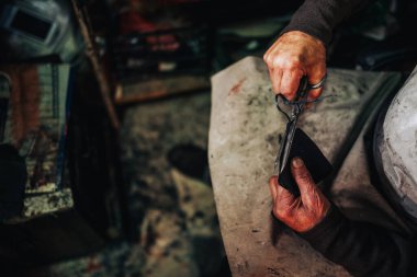 Ayakkabıcı 'nın ellerini kapat, deri parçalarını makasla kes ve ayakkabıcısının atölyesinde ayakkabı yapımına hazırla. Tanımlanamayan usta bir zanaatkar atölyesinde deri parçaları kesiyor.