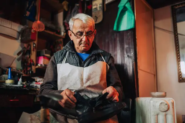 Ayakkabı tamirhanesinde oturup ayakkabı tamir eden yaşlı bir zanaatkârın portresi. Önlüklü usta bir zanaatkar dükkanında oturmuş eski botlarına bakıyor. Kıdemli adam eski botlarını yenisi kadar iyi yapıyor.