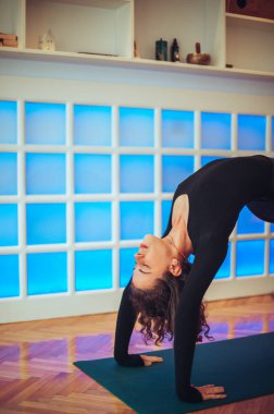 Güzel kıvırcık bir kızın, rahat stüdyosunda yoga yaparken briç pozu verirken yakın plan çekimleri. Nefes almaya konsantre olurken gözleri kapalı esnemenin tadını çıkarıyor. Boşluğu kopyala.