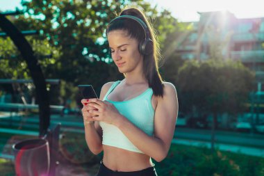 Parkta egzersiz yaparken müzik dinleyen genç bir kadının portresi.