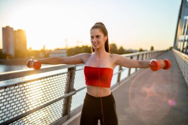 Gün batımında köprüde ağırlıklarla antrenman yapan güzel bir kadının portresi.