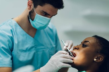 Afro-Amerikan bir kadın hastaya oral tedavi ve tıbbi hizmet sunan bir dişçinin fotoğrafı. Diş sağlığı kliniğinde diş kontrolü.