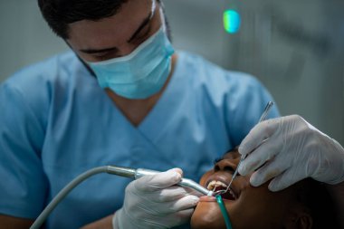 Hasta dişlerini incelerken steril ekipman kullanan uzman bir stomatolog. Afrikalı Amerikalı kadın hasta dişçi tarafından muayene ediliyor. Sağlık ve Tıp Konsepti.