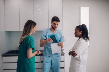 Doktor çene röntgenini tutuyor ve hastanedeki kadın meslektaşlarının yardımıyla ağız cerrahisi için teşhis koyuyor. Sorunlar tartışılıyor.