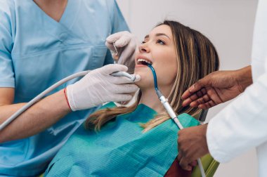 Dişçi kliniğinde bir kadın hastayla çalışan profesyonel erkek dişçi. Hasta dişlerini düzeltirken steril ekipman kullanan uzman stomatolog.