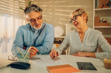 Olgun evli çift faturaları ödemek için faturaları kontrol ederken ya da belgeleri incelerken ve evde masada otururken. Ev giderlerini hesaplayan yaşlı eşler. Boşluğu kopyala.