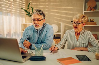 Önemli belgeleri okuyup evde dizüstü bilgisayar kullanan mutlu bir çift. Gülümseyen olgun eşler, internet üzerinden ödemeden önce yerli faturaları kontrol ediyor, bütçe planlamasını tartışıyorlar. Çevrimiçi bankacılık.