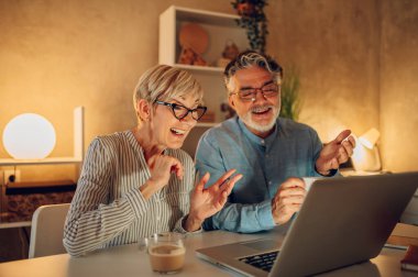 Yaşlı orta yaşlı mutlu çift evde video görüşmesi yaparken dizüstü bilgisayar kullanıyor. Gülümseyen yaşlı bir aile aile aile ya da arkadaşlarıyla konuşuyor. Yaşlılar ve teknoloji kavramı. Boşluğu kopyala.