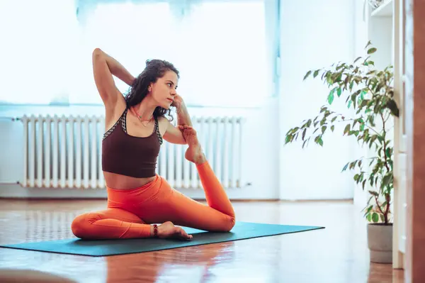 stock image Wide shot of a beautiful caucasian girl doing her morning stretch while bending her legs at the knees and leaning back.Sitting on a yoga mat on a cozy yoga studio and enjoying her practice.Copy space.