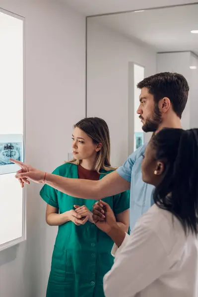 stock image Group of doctors looking at x-ray image from jaw while working in a hospital. Multiracial oral surgeons. Healthcare, medical and radiology concept.