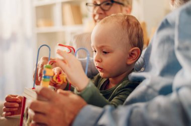 Yaşlı çift torunlarıyla kanepede kaynaşırken o da evdeki kanepede oyuncaklarla oynuyor. Bebek bakıcılığı. Evde tahta oyuncakla oynayan güzel bir çocuğun portresi. Boşluğu kopyala.