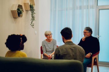 Grup terapisine katılan çok ırklı yetişkinler grubu. Destek grubu toplantısında kıdemli erkek ve kadınlar. İncinebilirlik, toplum ve akıl sağlığı. Olgun bir bayana odaklan. Boşluğu kopyala.