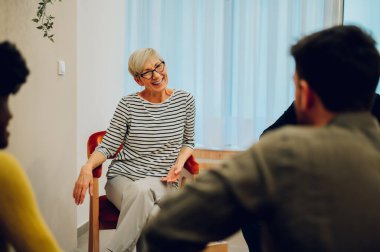 Grup terapisine katılan gülümseyen yaşlı kadın. Destek grubundaki çeşitli erkek ve kadınlar olgun kadınların hikayesini dinliyor. İncinebilirlik, toplum ve akıl sağlığı. Boşluğu kopyala.