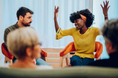 Elleri havada Afrikalı Amerikalı bir kadın grup terapisine katılırken diğer hastalarla sorunlarını tartışıyor. Psikolojik rehabilitasyon sırasında hikayeler anlatmak. Boşluğu kopyala.