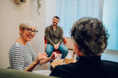 Grup terapisine katılan ve kutudan mendil alan yaşlı bir kadının portresi. Çeşitli erkek ve kadınlar grup toplantısındalar. İncinebilirlik, toplum ve akıl sağlığı. Boşluğu kopyala.
