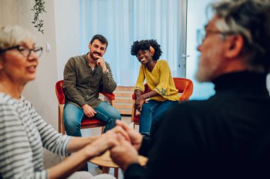 Akıl sağlığı merkezindeki bir toplantıda gülümseyen ve diğer insanları dinleyen farklı insanların portresi. Grup terapisi katılımcıları bir çemberin içinde oturup konuşuyorlar. Boşluğu kopyala.
