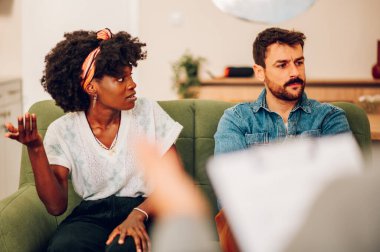 Mutsuz ve çeşitli çiftler ofiste evlilik terapistiyle psikoterapi görüyorlar. Çok ırklı bir çift terapide sorunlar hakkında konuşuyor. Evlilik terapisi. Boşluğu kopyala.