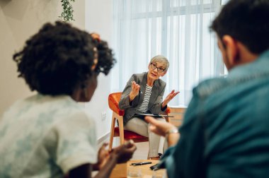 İlgili olgun kadın doktor, müşterilerinin zihinsel ve evlilik problemlerini not alırken dinliyor. Psikoterapi danışmanlığı. Boşluğu kopyala.