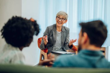 İlgili olgun kadın doktor müşterilerinin zihinsel ve evlilik problemlerini dinliyor ve not alırken ofisinde not alıyor. Psikoterapi danışmanlığı. Boşluğu kopyala.