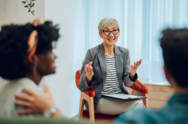 Gülümseyen ve ilgili olgun bir kadın doktorun portresi müşterilerinin zihinsel ve evlilik problemlerini not alırken dinliyor. Psikoterapi danışmanlığı. Boşluğu kopyala.