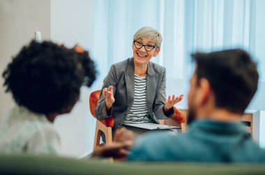 Ofiste terapi seansı sırasında hastalarıyla konuşan kıdemli kadın psikiyatrist. Akıl sağlığı danışmanı. Psikoterapi danışmanlığı.