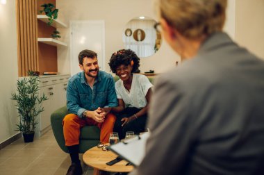 Ofiste terapistle psikoterapi seansı yapan mutlu çift. Çok ırklı bir çift terapide sorunlar hakkında konuşuyor. Başarılı bir evlilik terapisi. Gülümseyen melez çift.