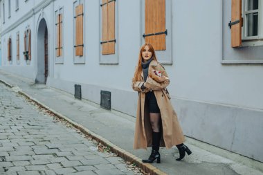 Kızıl saçlı modaya uygun genç bir kadın eski bir kasaba caddesinde beklerken elinde bir buket çiçek tutuyor. Eski moda elbiseli bir kadın kaldırım taşlı, elinde çiçek buketi olan eski moda bir sokakta bekliyor..