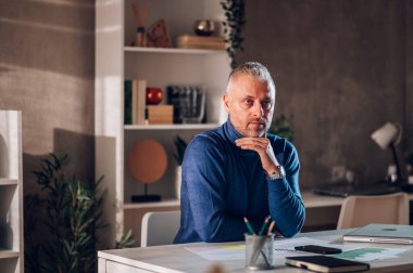 Evde çalışan başarılı orta yaşlı girişimci portresi. Yakışıklı orta yaşlı işadamı ev ofisinde çalışırken başka tarafa bakıyor ve iş sorununa çözüm düşünüyor..