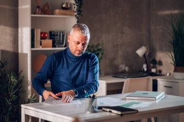 Yakışıklı, orta yaşlı, evde uzaktan çalışan ve bir ofis masasında otururken bazı iş belgelerini ve sözleşmeleri gözden geçiren bir serbest çalışan. İş ve serbest çalışma. Boşluğu kopyala.