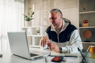 Modern işyerindeki bilgisayarında çalışan orta yaşlı bir adam. Gri sakallı ve saçlı bir iş adamı. Ev ofisinin modern bir çalışma yerinde uzaktan çalışıyor. Boşluğu kopyala.