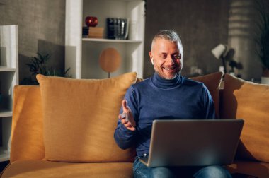 Müşterileri, arkadaşları ve ailesiyle video görüşmesi yaparken dizüstü bilgisayarda çalışan mutlu orta yaşlı bir adamın portresi. Yakışıklı bir adam uzaktan insanları laptop kamerasıyla arıyor..