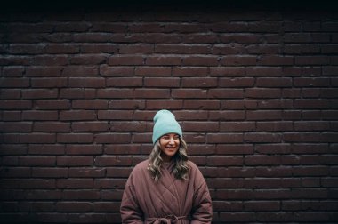 Tuğla duvarın önünde poz veren güzel, şık bir kadın.