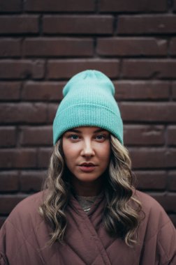 Tuğla duvarın önünde poz veren güzel, şık bir kadın.