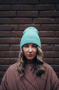 Tuğla duvarın önünde poz veren güzel, şık bir kadın.