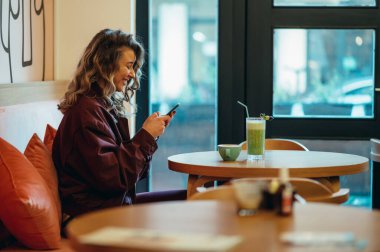 Matcha latte kahve içen ve kafede akıllı telefon kullanan güzel genç bir kadın.
