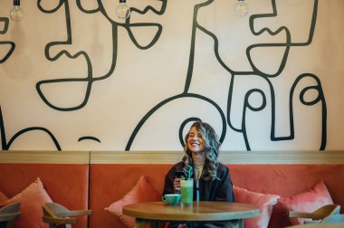 Kahve içen ve kafede akıllı telefon kullanan güzel genç bir kadın.