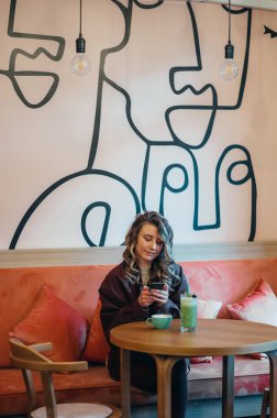 Kahve içen ve kafede akıllı telefon kullanan güzel genç bir kadın.