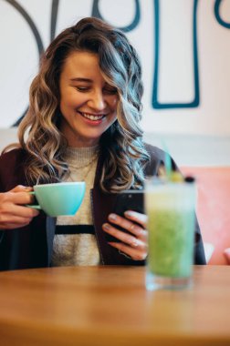 Kahve içen ve kafede akıllı telefon kullanan güzel genç bir kadın.