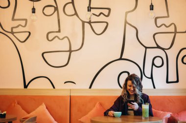 Kahve içen ve kafede akıllı telefon kullanan güzel genç bir kadın.