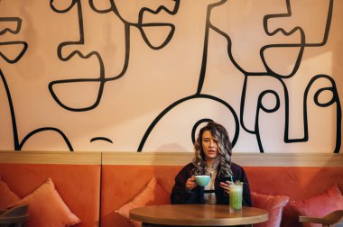 Kahve içen ve kafede akıllı telefon kullanan güzel genç bir kadın.