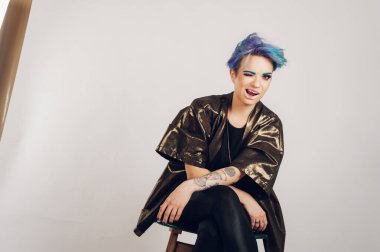 Stüdyoda beyaz bir arka planda renkli makyajlı güzel bir kız. Moda, güzellik, makyaj, kozmetik. Makyajlı kadın modelin güzel portresi. Sandalyede oturan ve göz kırpan bir kadın.