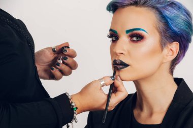 Makyaj sanatçısı elleriyle canlı makyajlı neşeli, kısa saçlı bir kadının portresi. Beyaz arka planda poz veren kadın model. Güzel bir kadın yüzü. Güzellik modeli konsepti.