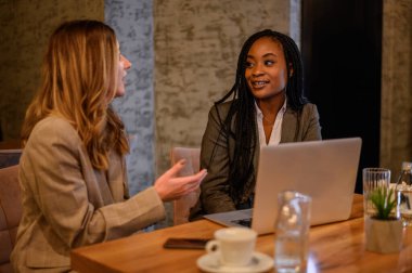 İki iş kadını bir kafede dizüstü bilgisayar kullanırken buluşuyorlar.