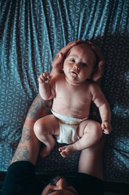 Dövmeli sakallı baba evde yatağında oğluyla oynarken bez takıyor.